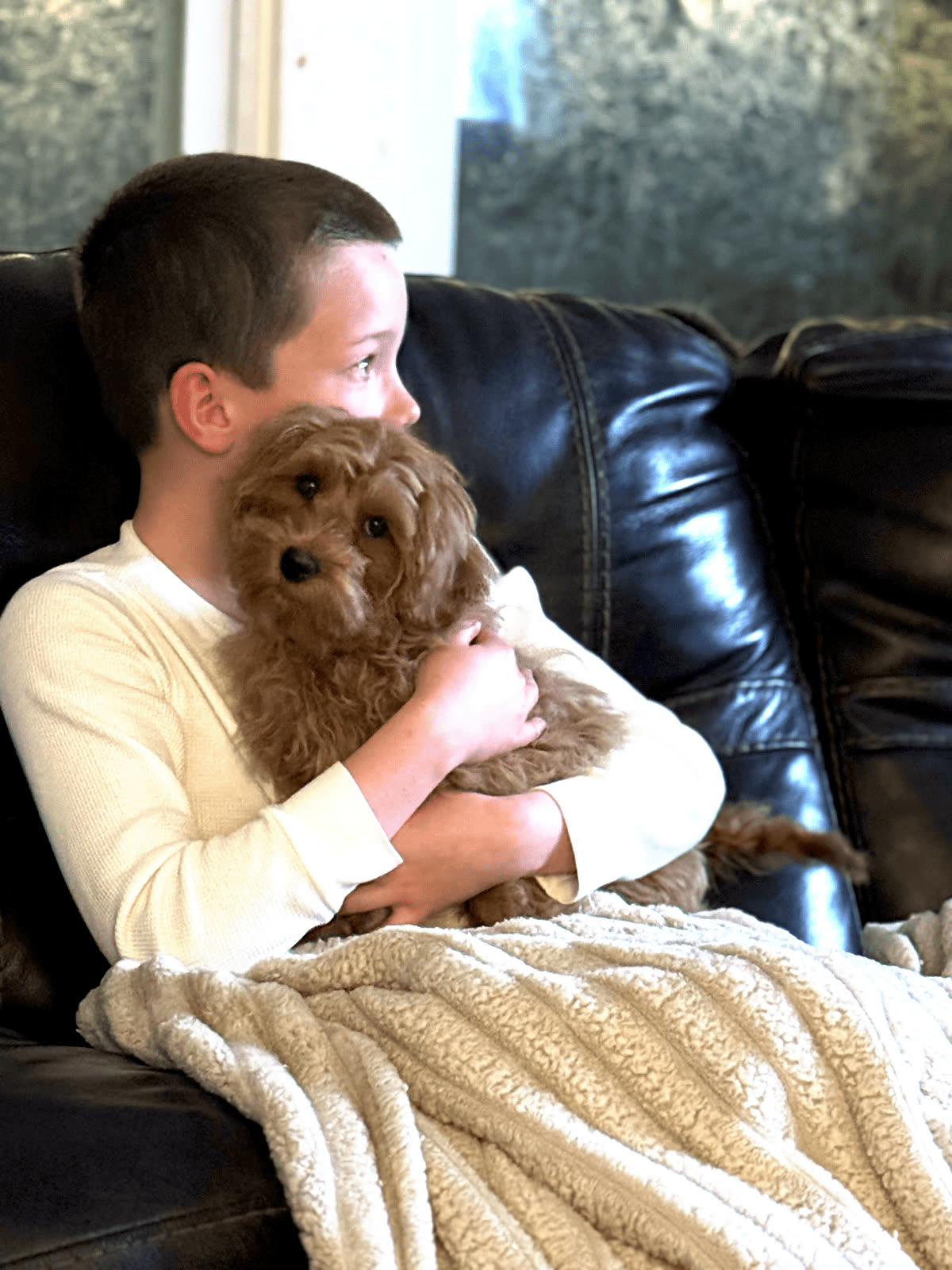 A child holding a puppy while sitting on a couch